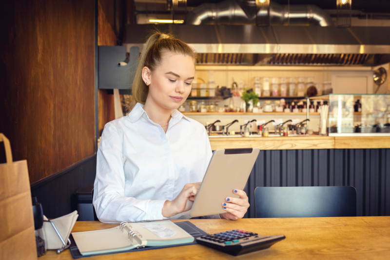 Une jeune femme d'affaires est assise à la table d'un café et consulte les données relatives à la fidélisation de la clientèle sur une tablette portable.