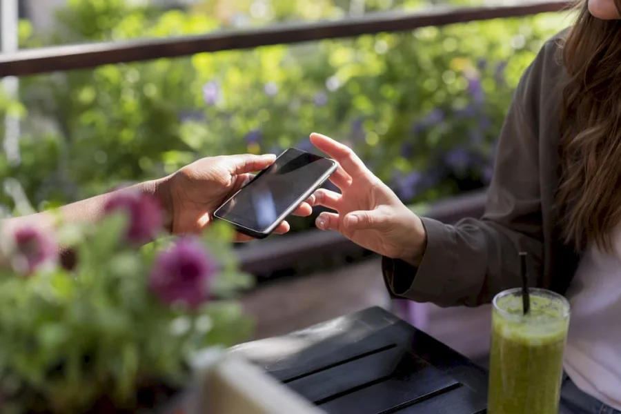 Mano realizando una transferencia de puntos en un tel&eacute;fono m&oacute;vil en una cafeter&iacute;a