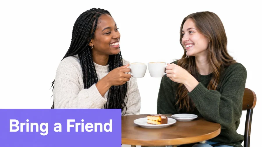 Two female friends smiling and toasting with coffee mugs over a slice of cake at a table.
