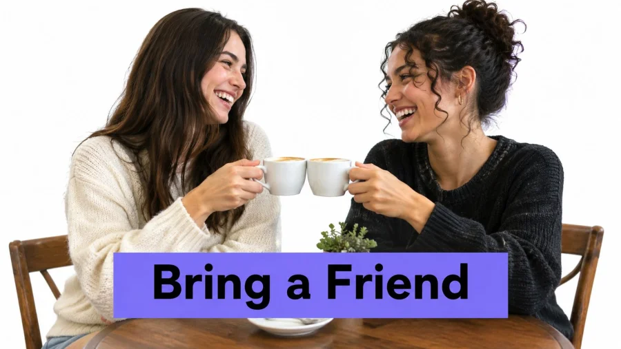 Two happy women laughing and clinking coffee cups while sitting at a wooden table together.